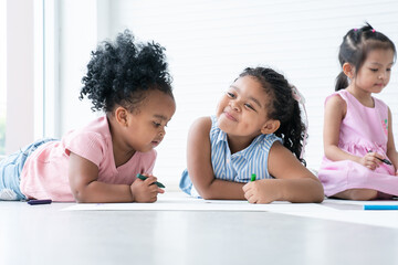 African cute little kids girls have fun drawing on paper while sitting and lying on the floor with friends. Adorable happy children drawing with colorful crayons at preschool. Education concept