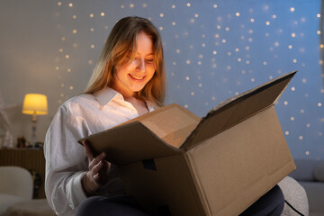 girl unpacks a parcel in the evening, unpacking a mysterious box, online shipping, parcel delivery...