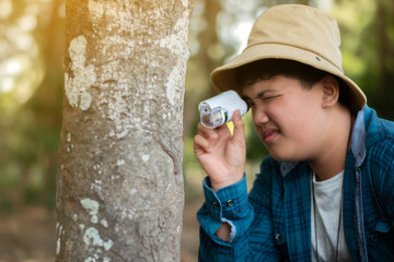 Asian boy using outdoor portable microscope to watch moss pattern which growing on tree trunk...