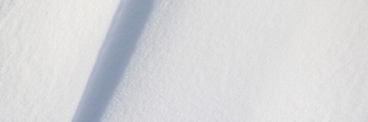 Beautiful winter background with snowy ground. Natural snow texture. Wind sculpted patterns on snow surface. Wide panoramic texture for background and design. Closeup top view with copy space.