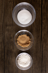 Obraz na płótnie Canvas sugar, brown sugar, and flour in glass bowls against wood