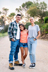 vertical photo looking at camera of a father, mother and daughter smiling happy in the countryside, concept of active tourism in nature and family outdoors activities