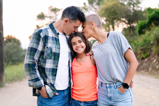 portrait in the countryside of a father and mother kissing their daughter who smiles happily looking at camera, concept of active tourism in nature and family outdoors activities
