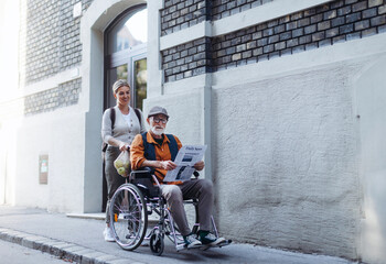 Granddaughter pushing senior man in wheelchair on street. Female caregiver and elderly man enjoying a warm autumn day, going home from shopping.