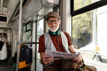 Elderly man traveling through the city by bus, reading newspaper. Senior city commuter taking tram...