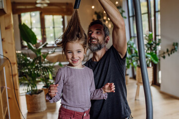 Father vacuuming girl's hair with vacuum cleaner. Father and daughter cleaning the house, helping...