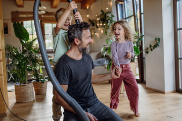 Father and kids cleaning house, vacuuming the floors with a vacuum cleaner. Young boy and girl helping with house chores. - obrazy, fototapety, plakaty