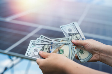 saving concept man hold dollar against photovoltaic solar panels
