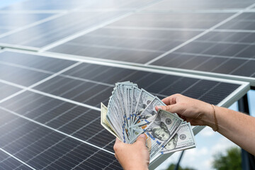 saving concept man hold dollar against photovoltaic solar panels
