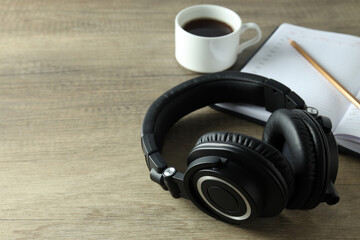 Black big headphones, on a table with a notebook and coffee.