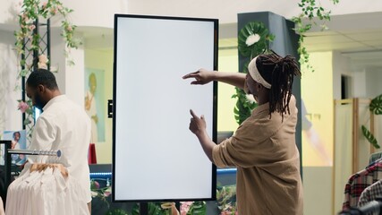 African american man in clothing store using augmented reality mockup screen to look at garment...