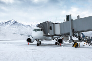 White passenger jet plane at the airgate at winter airport apron on the background of high...