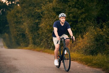 Obraz premium A young and fit cyclist on a bicycle explores the country landscape, riding on a road in the forest with a helmet and a mountain bike. Gravel biker on a path, enjoying the sport and the nature.