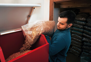 A bearded man using wood pellets as a renewable and eco-friendly fuel source for his boiler,...