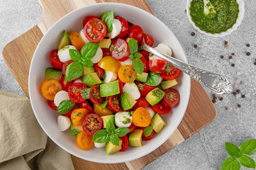 Caprese salad with cherry tomatoes, mini mozzarella balls, avocado, pesto sauce and fresh basil. Healthy vegetarian meal.