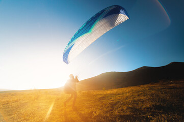 paraglider above the ground is preparing to fly. A professional athlete raised his parachute over a...
