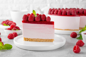 No baked raspberry cheesecake or raspberry cream mousse cake with jelly and fresh berries on top on a white plate on a gray concrete background. Summer cake. - obrazy, fototapety, plakaty