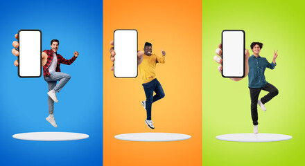 Cheerful young diverse men show big smartphone with blank screen, jump at platform, have fun