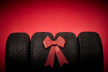 Car tires, new tyres, winter wheels isolated on red christmas background with bow ribbon present