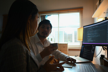Male and female software developers discussing and programming on desktop computer - obrazy, fototapety, plakaty