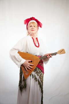 Cheerful funny adult mature woman solokha with musical balalaika. Female model in clothes of national ethnic Slavic style. Stylized Ukrainian, Belarusian or Russian woman poses in a comic photo shoot