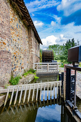 Water canal at old Eper or Wingbergermolen water mill, next of Geul river, fence, wooden bridge and trees against blue sky in background, sunny day in Terpoorten, Epen, South Limburg, Netherlands © Emile