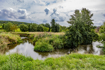 Dutch countryside landscape with winding Geul river among wild vegetation, hills with leafy trees...