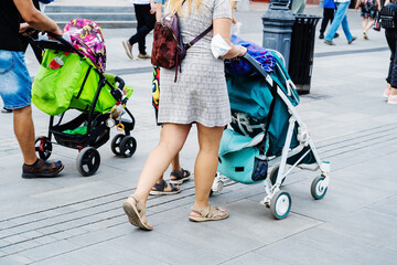 A woman and a man with baby strollers are walking along a busy street. Parents with young children...