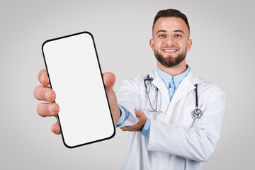 Man doctor with big phone, blank screen on grey background
