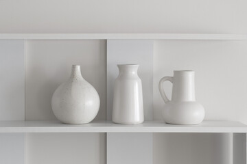 Fototapeta na wymiar white ceramic vases on wooden shelf on white wall