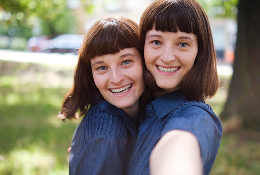 Smiling twin sisters taking selfie in park
