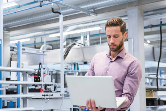 Young engineer working on laptop at factory
