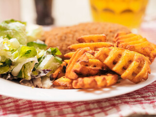 Southern fried chicken fillet meal with green fresh salad and fancy cut potato chips served on white plate and glass of lager beer. Simple tasty food to eat. Selective focus.