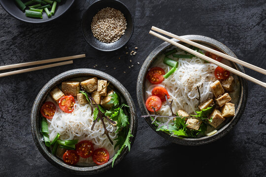 Bowls of vegan Tom kha kai soup with tofu, tomatoes, salad, rice noodles, sesame seeds and scallion