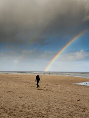 Nature scene with beach, ocean and cloudy sky with rainbow. Silhouette of people walking on the sand. Rich saturated colors. Nature wonder scene. West of Ireland.