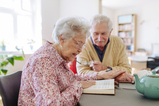 Senior man with woman reading book and holding hands at table