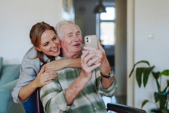 Smiling healthcare worker hugging senior man taking selfie at home