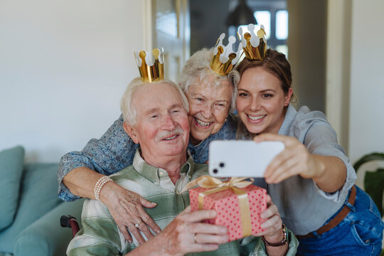 Happy healthcare worker taking selfie with senior couple and celebrating birthday at home - Powered by Adobe