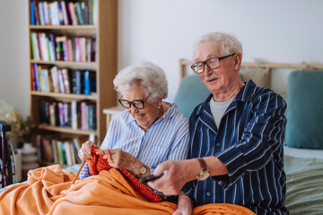 Happy senior woman knitting with man holding remote and watching TV at home
