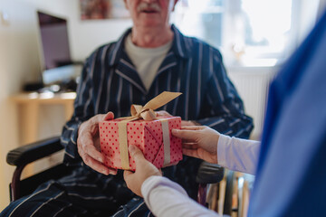 Hands of healthcare worker giving gift to senior man at home