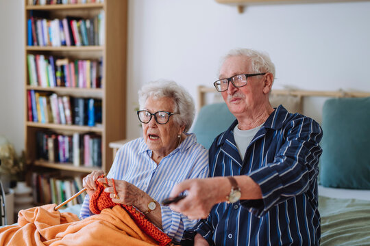 Senior woman knitting with man holding remote and watching TV at home