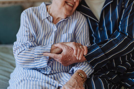 Happy senior woman holding hands with man sitting on bed at home