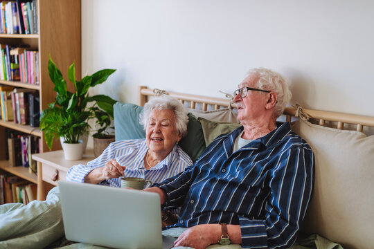 Smiling senior man and woman sitting with laptop on bed at home