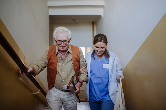 Smiling healthcare worker moving up with senior man on staircase at home