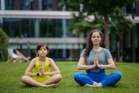 Mother and daughter spending together time outdoors practicing yoga in the city park