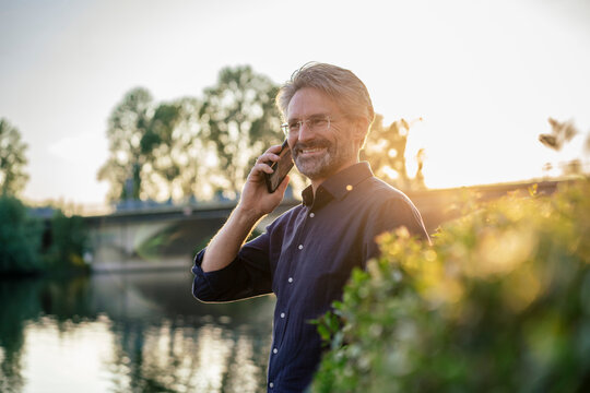 Happy man talking on smart phone near lake at sunset