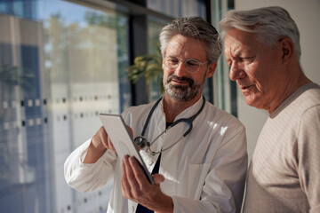 Senior doctor discussing with man over tablet PC in hospital