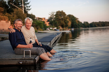 Smiling senior friends sitting on pier with beer bottles