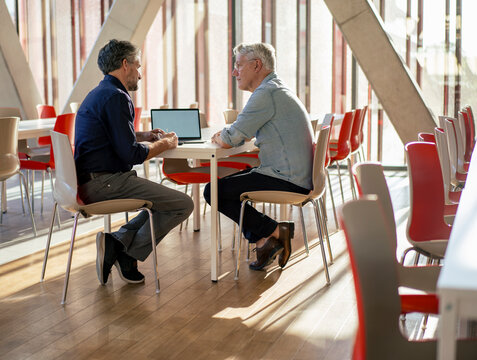 Senior businessman discussing with colleague over laptop at table in cafeteria