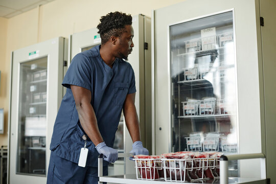 Lab technician holding trolley looking at fridge with blood bags